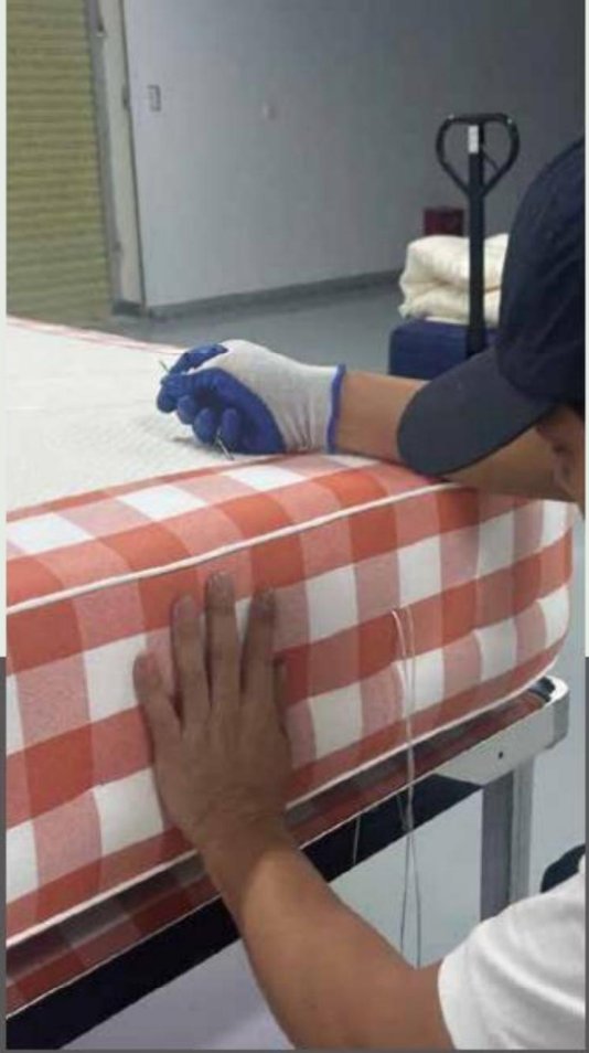 Artisan hand-pressing the checkered side wall of a mattress